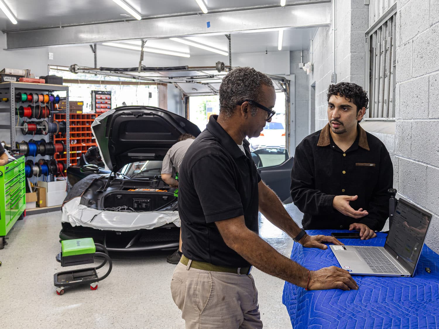 AliNQuality founder discussing a workflow with a client beside a laptop at the client's business
